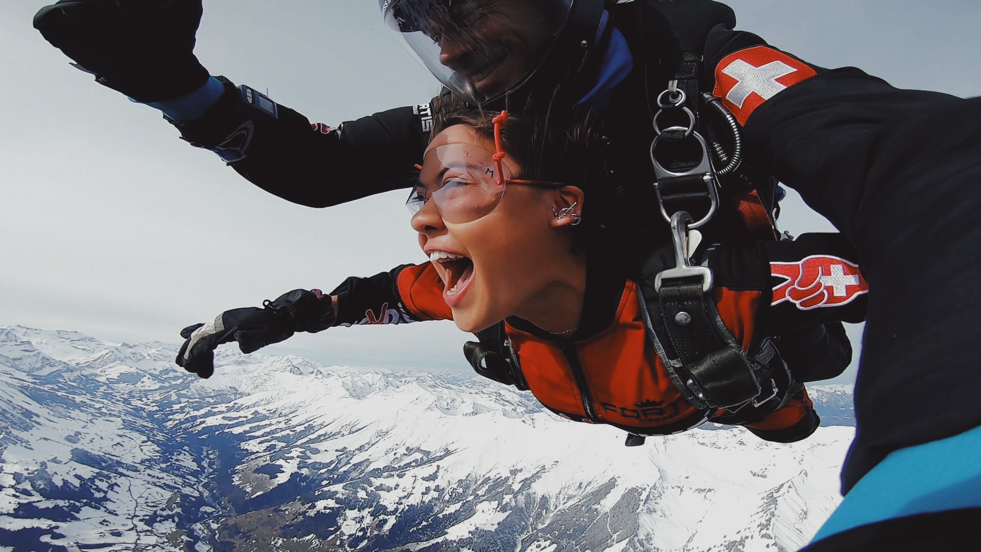 young brunette girl tandem skydiving with instructor over swiss alps